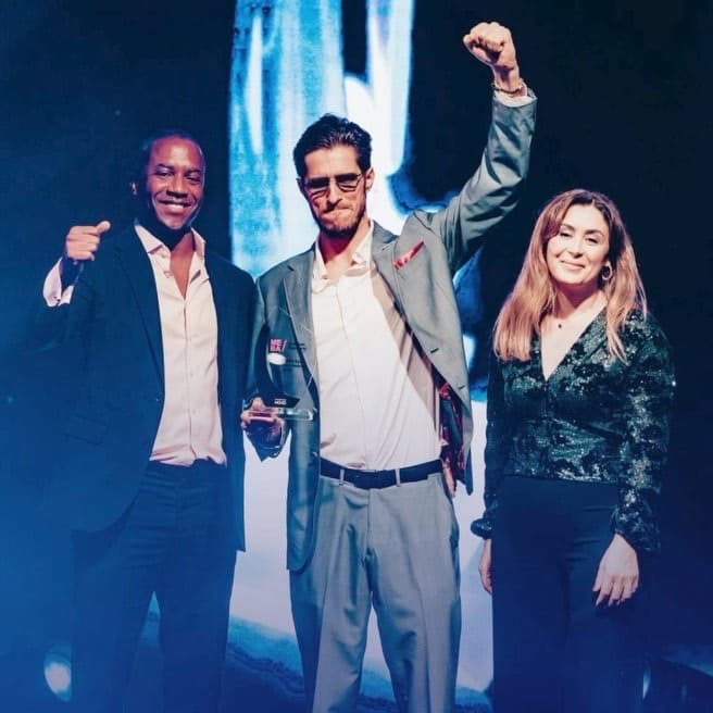 Matthias Mende raising a fist on stage holding the MEBA award