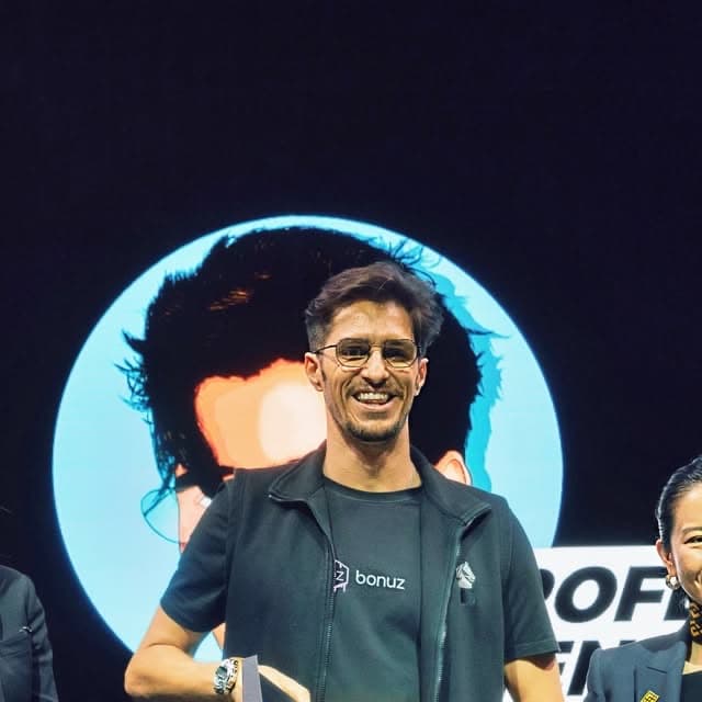 Matthias Mende smiling on stage in a bonuz shirt at Binance Blockchain Week